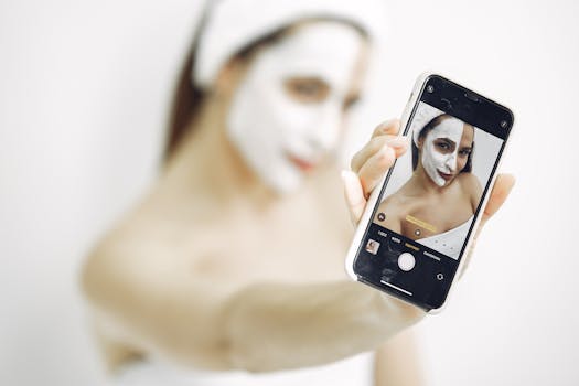 A woman captures a selfie using a smartphone while wearing a facial mask indoors.