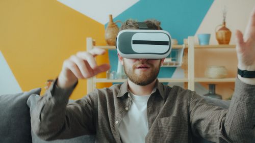 Free Bearded man using virtual reality headset at home, exploring digital worlds. Stock Photo