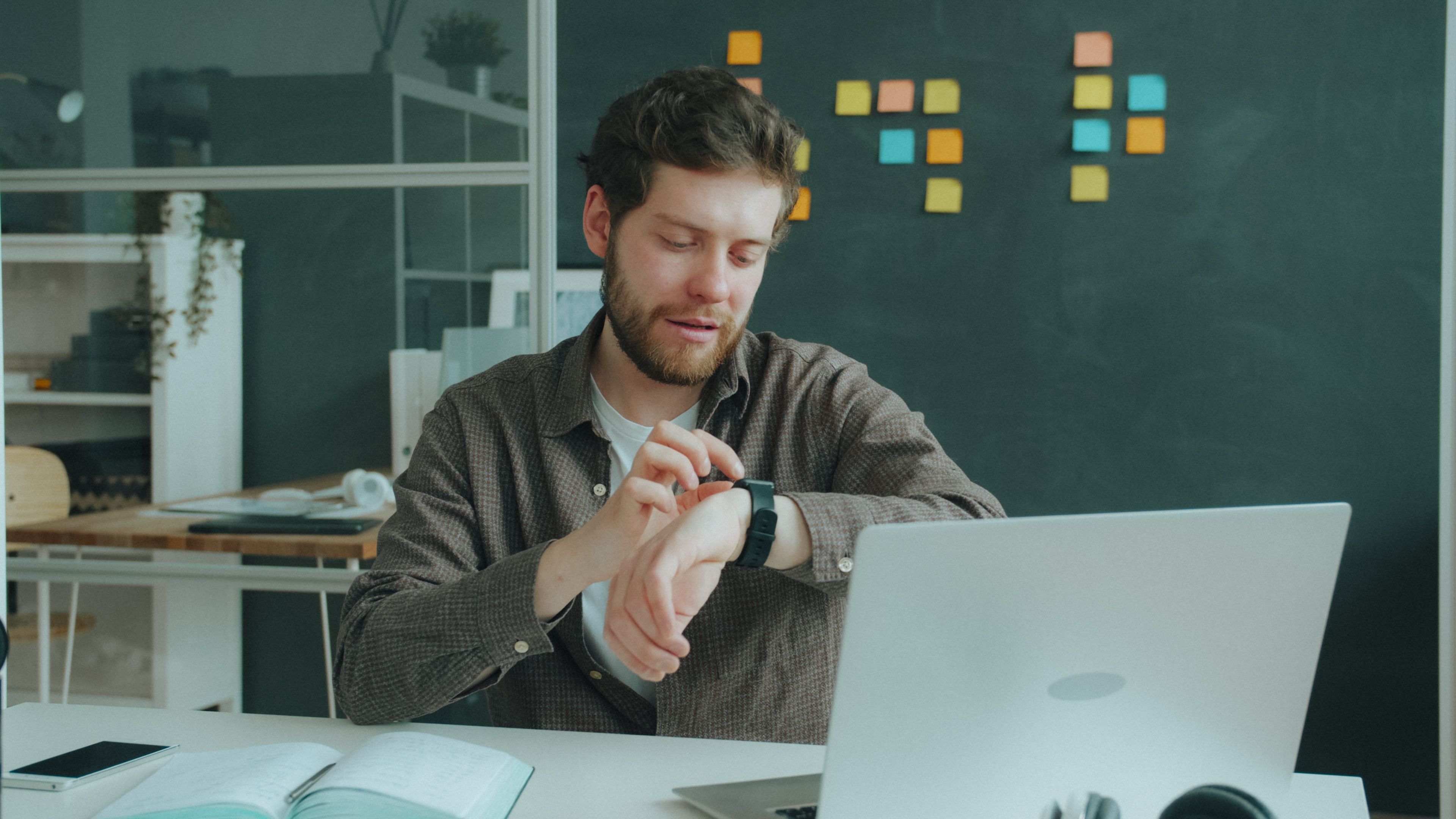 Man checks smartwatch while working at a laptop in a modern office setting.