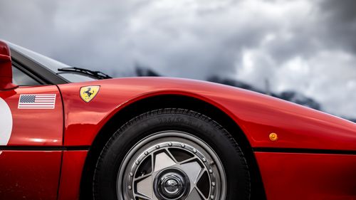 Free Detailed view of a red sports car's wheel and badge under a dramatic cloudy sky. Stock Photo