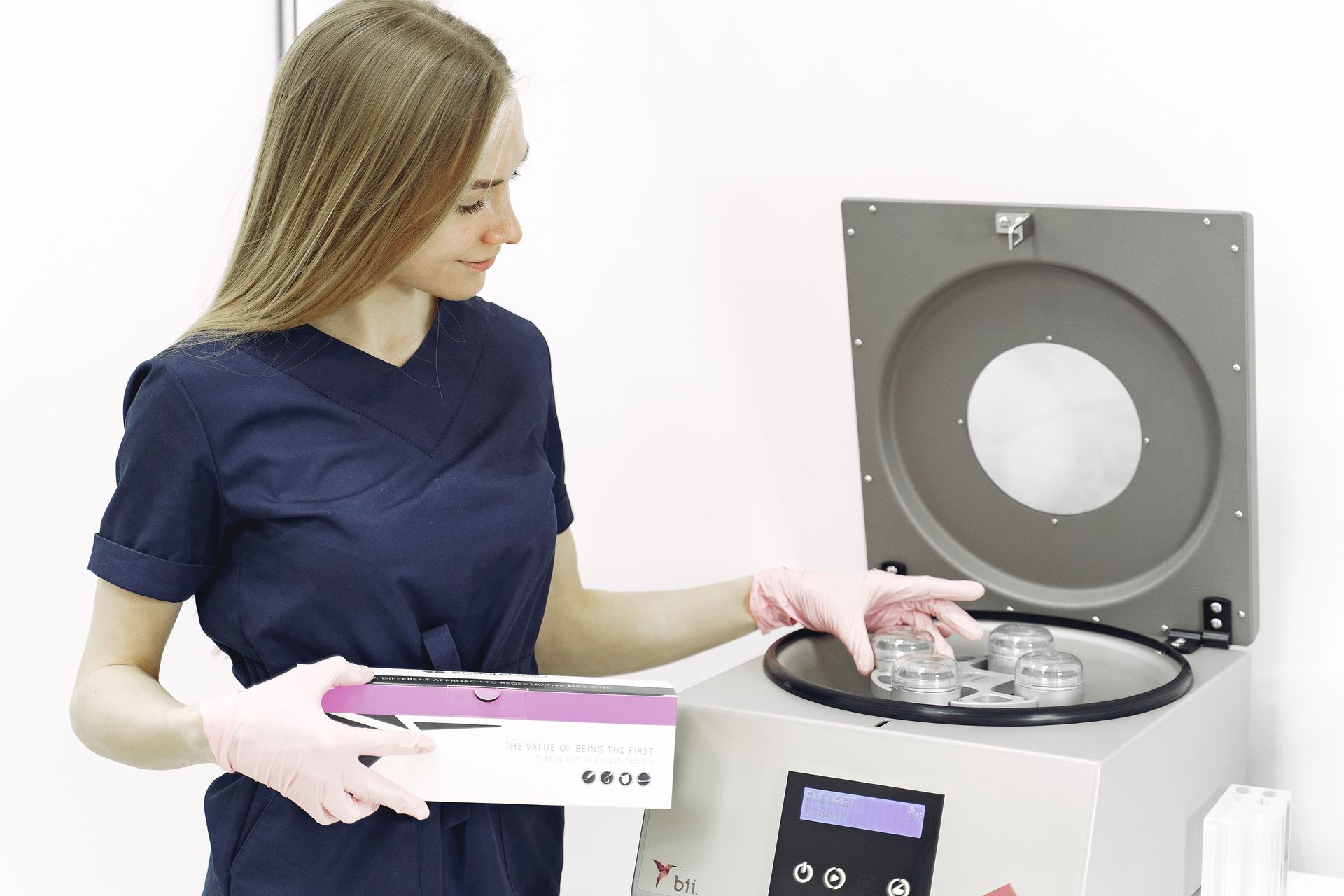 A healthcare worker using a centrifuge in a clinical setting, wearing gloves and scrub suit.