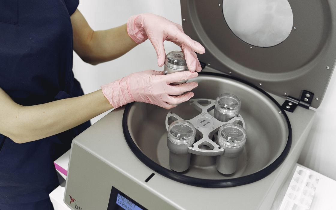 Gloved clinician placing sample holders into a centrifuge used to prepare platelet-rich plasma