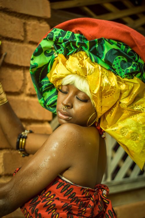 Free Close-up portrait of a woman in colorful African attire and headwrap, enjoying the outdoors. Stock Photo