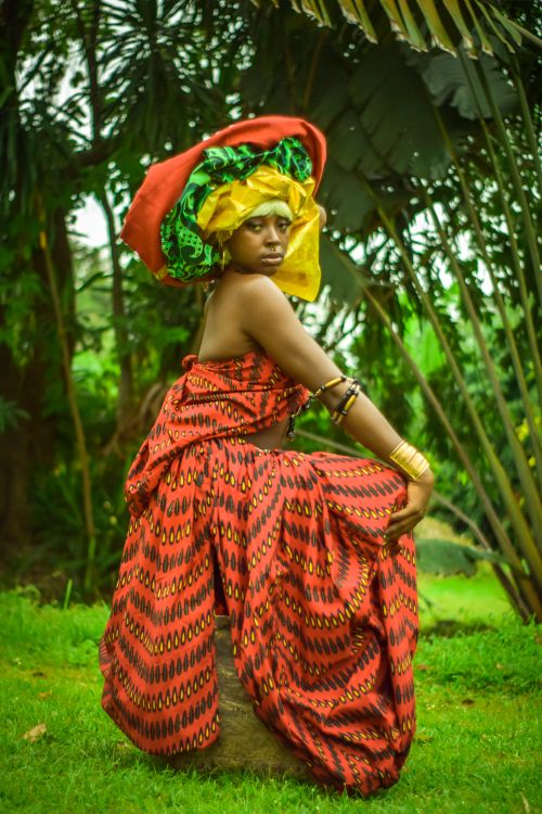 Free A young woman poses in colorful traditional African attire amid lush tropical greenery. Stock Photo