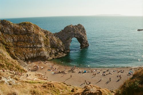 Free Aerial view of Durdle Door beach with iconic arch and sunbathers on a sunny day. Stock Photo