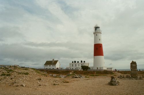 Free A scenic view of Portland Bill Lighthouse, England, surrounded by rugged terrain under a cloudy sky. Stock Photo