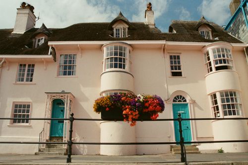 Free Picturesque pink house with vibrant flower basket and blue doors in Lyme Regis, England. Stock Photo