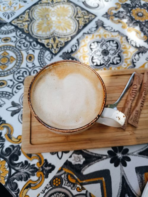 Free A foamy cappuccino on a wooden tray against a detailed, ornate tablecloth design. Stock Photo