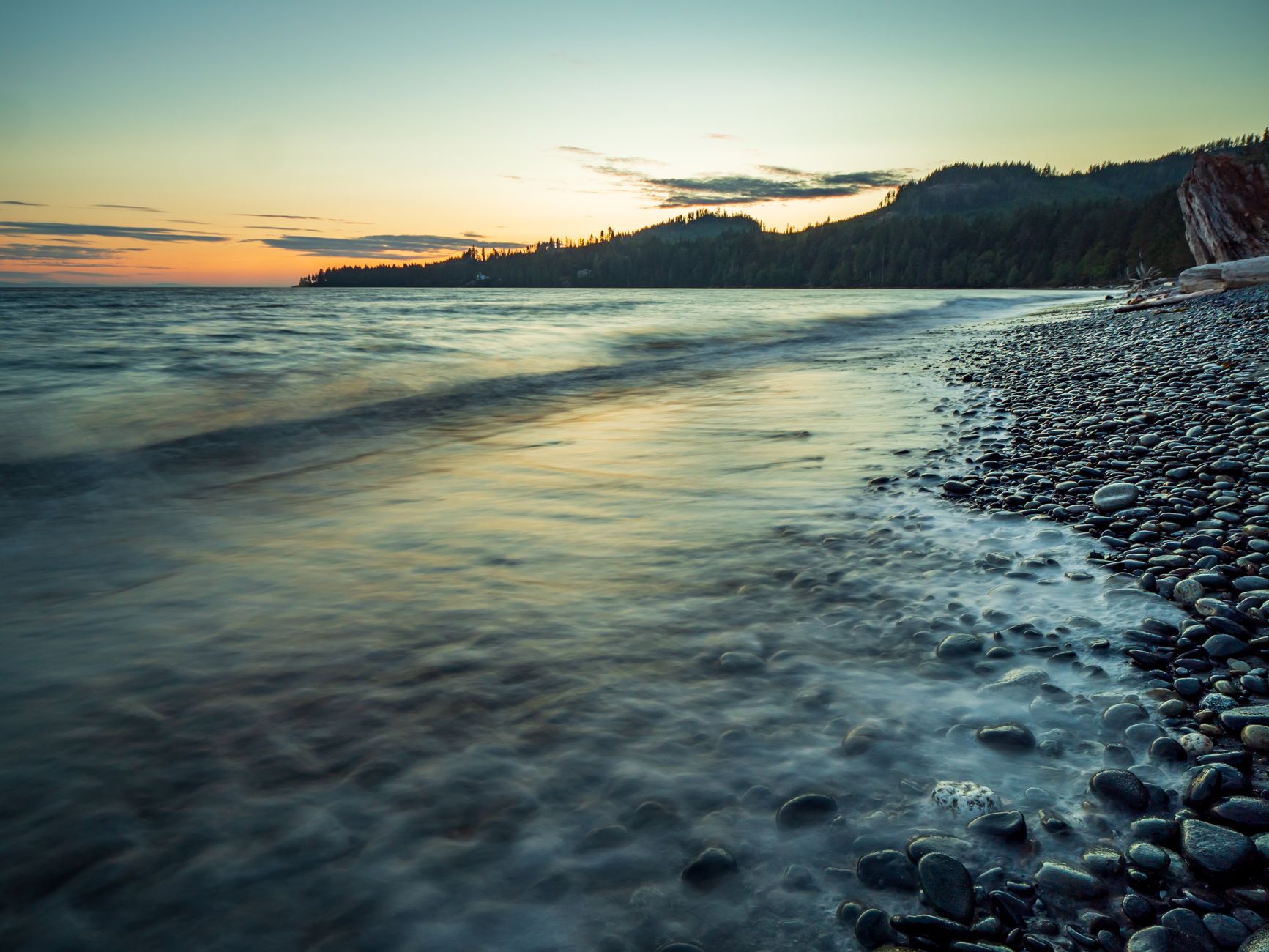 Tranquil sunset over a pebbled shoreline in British Columbia, Canada, capturing the coast's serene beauty. โ photo by James Wheeler / Pexels