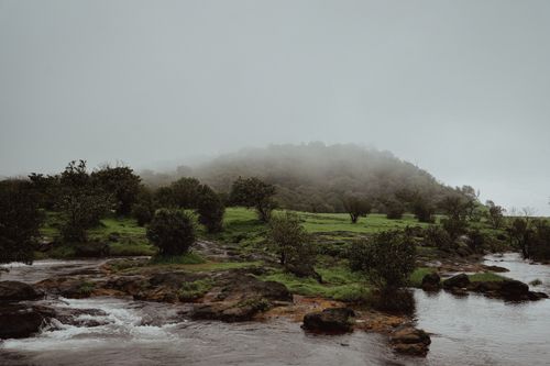 Free Serene misty landscape featuring a flowing river and lush green hills. Stock Photo