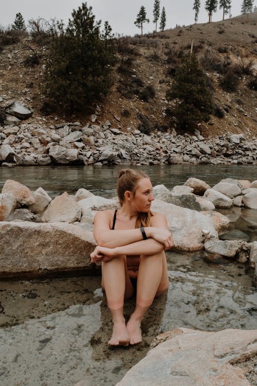 Pensive tourist resting in shallow river near stones during vacation