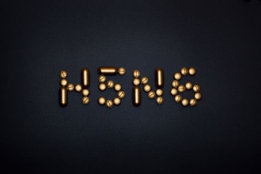 Gold pills on a black surface spell out H5N6, symbolizing medication or virus treatment.