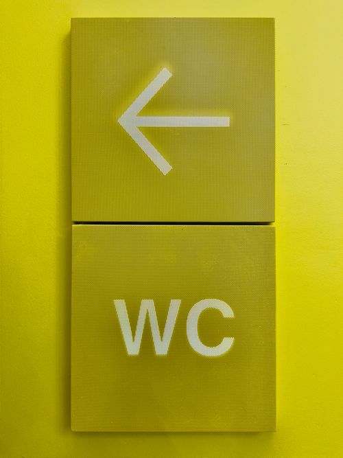 Free A vibrant yellow sign with an arrow pointing left and 'WC' indicating restroom direction. Stock Photo