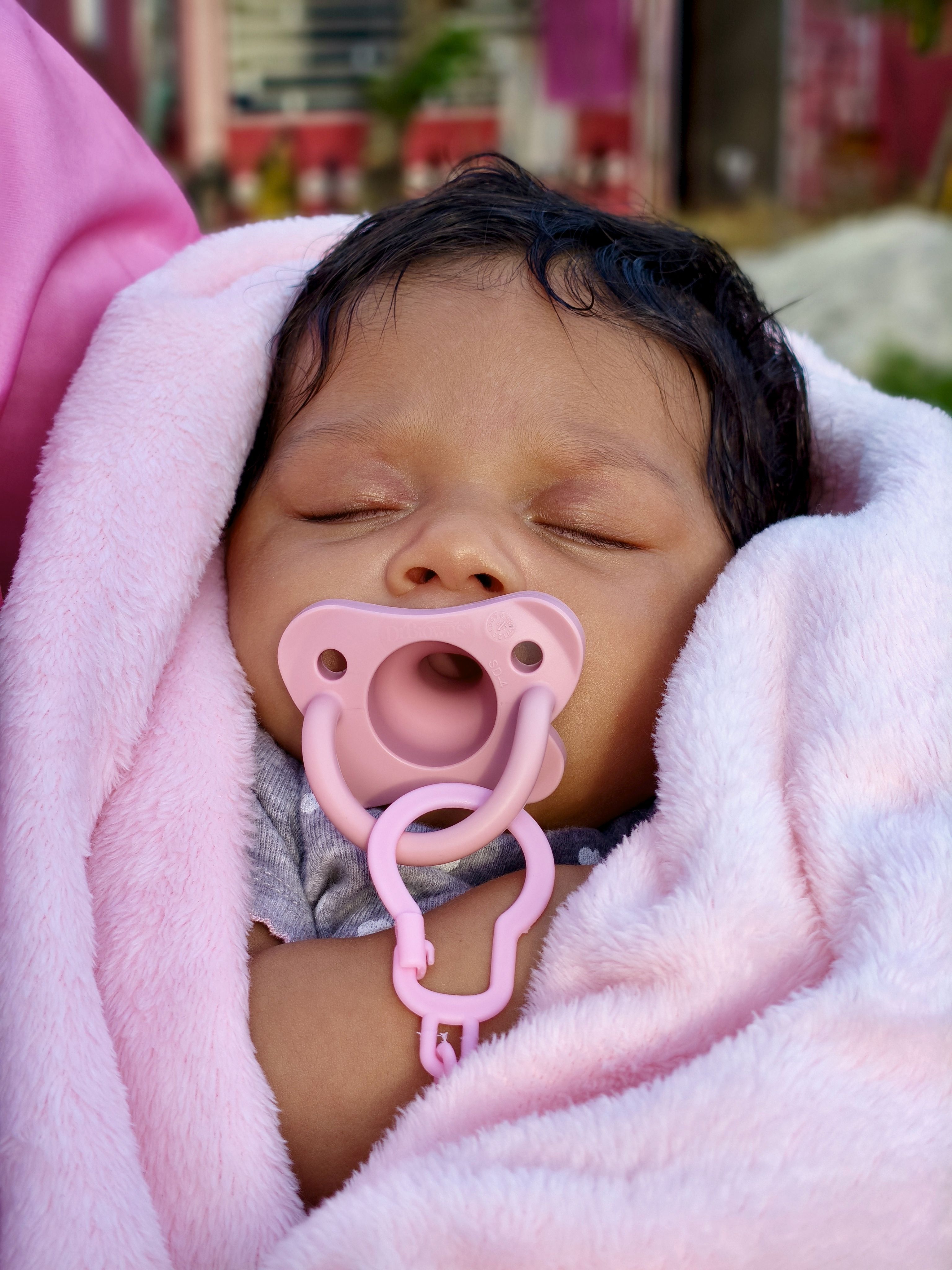 A peaceful baby wrapped in a pink blanket, sleeping with a pacifier in a serene outdoor setting.