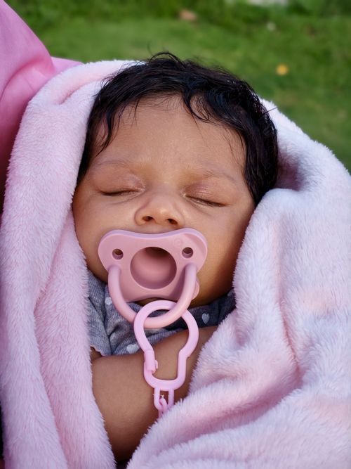 Free Peaceful sleeping baby wrapped in a soft pink blanket with a pacifier. Stock Photo