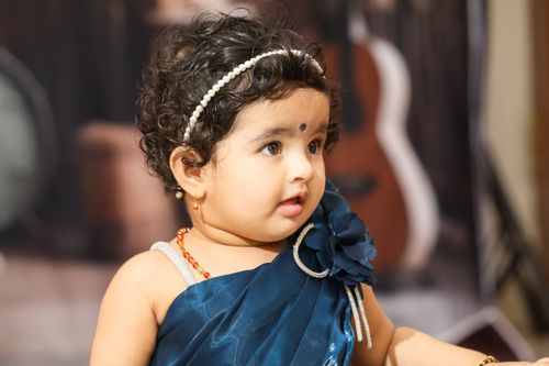 Free Adorable baby girl in a blue dress, adorned with pearl headband, looking curious. Stock Photo