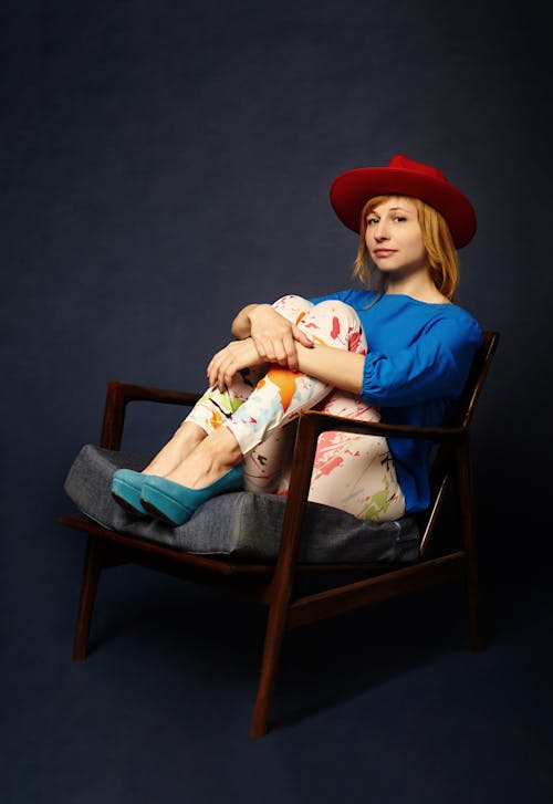 Woman In Blue Top And Red Hat Sitting On Armchair