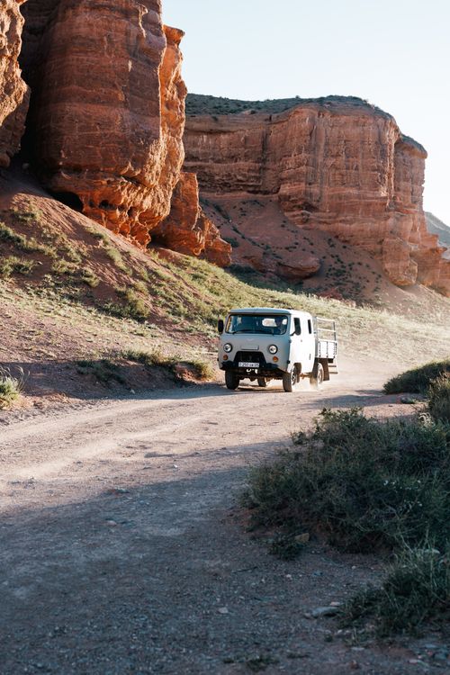 Free A white truck drives through the rugged landscape of Charyn Canyon in Kazakhstan, showcasing natural sandstone formations. Stock Photo