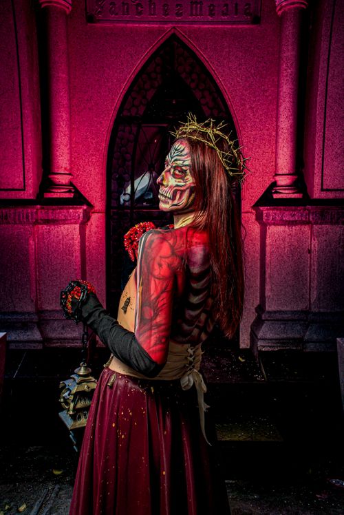 Free Striking portrait of a woman in vibrant skull makeup in a dimly lit, gothic cemetery setting. Stock Photo