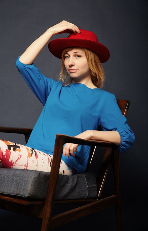 Woman In Blue Top And Red Hat Sitting On Chair