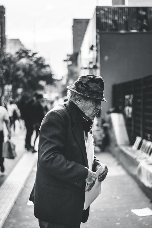 Free A senior man in a suit and hat walks along a busy city street in monochrome. Stock Photo
