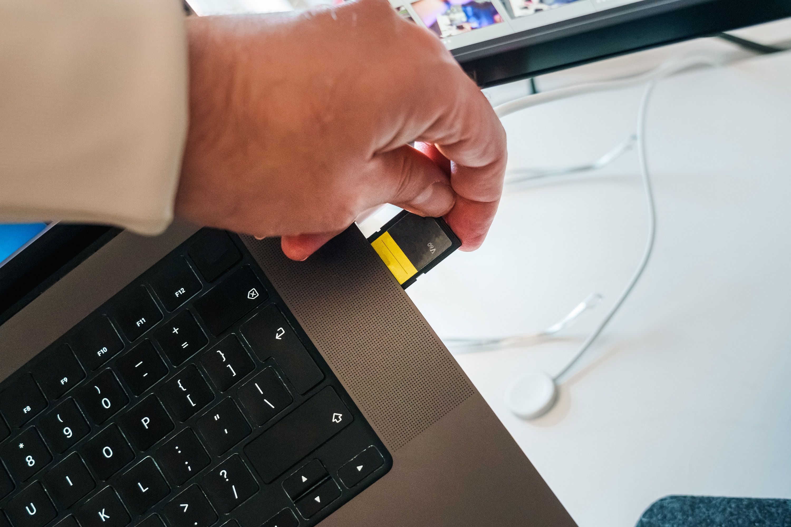 Close-up of a hand inserting an SD card into a laptop, highlighting tech and data transfer.