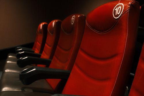 Free Row of plush red cinema seats with armrests in a dimly lit theater. Stock Photo