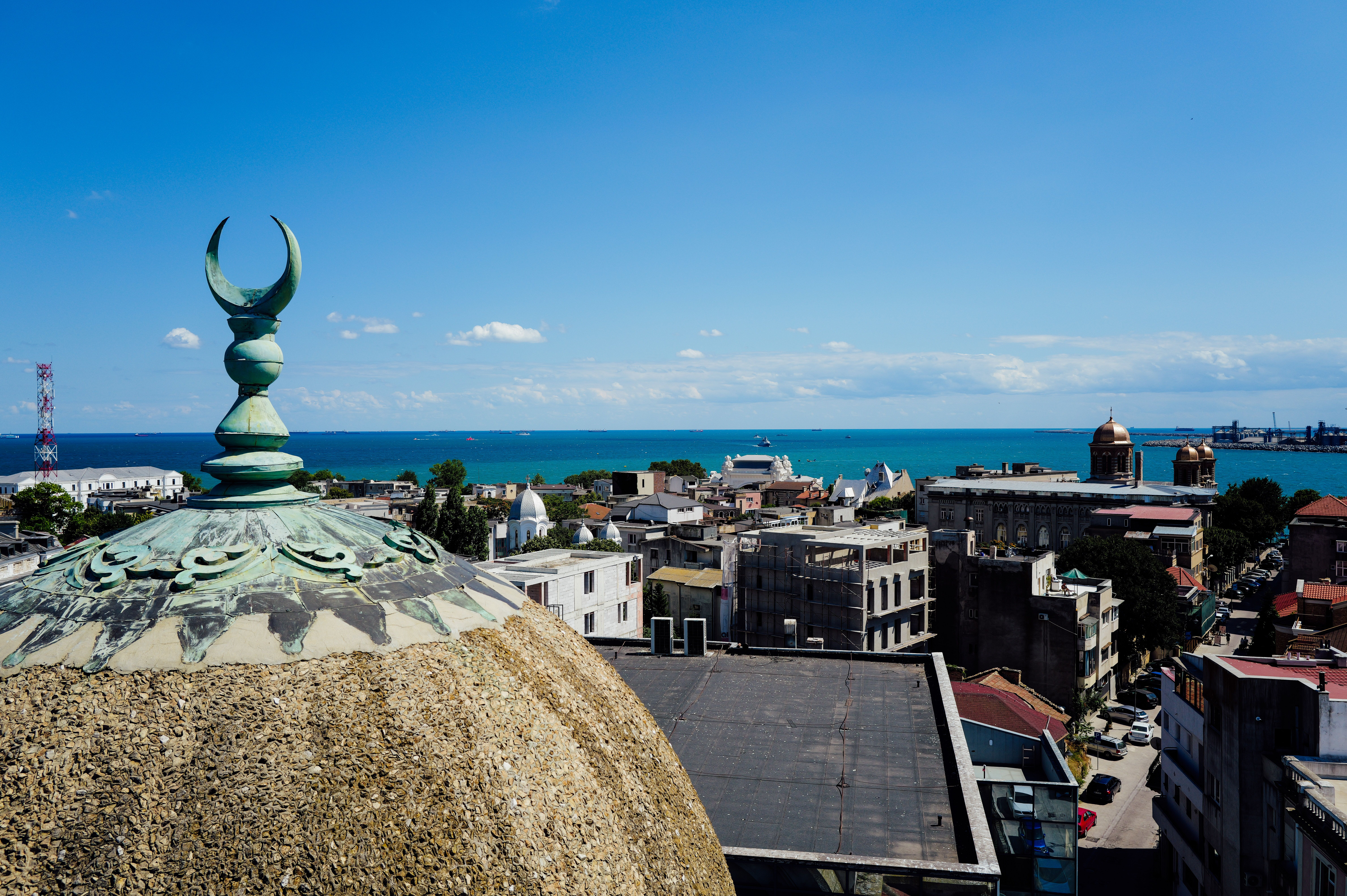 Scenic view of a coastal city with a mosque dome and crescent against a blue sky.