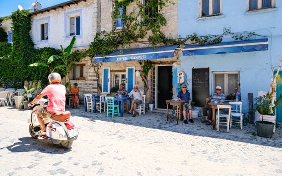 A vibrant street cafe with locals and a scooter passing in a sunny Turkish village.