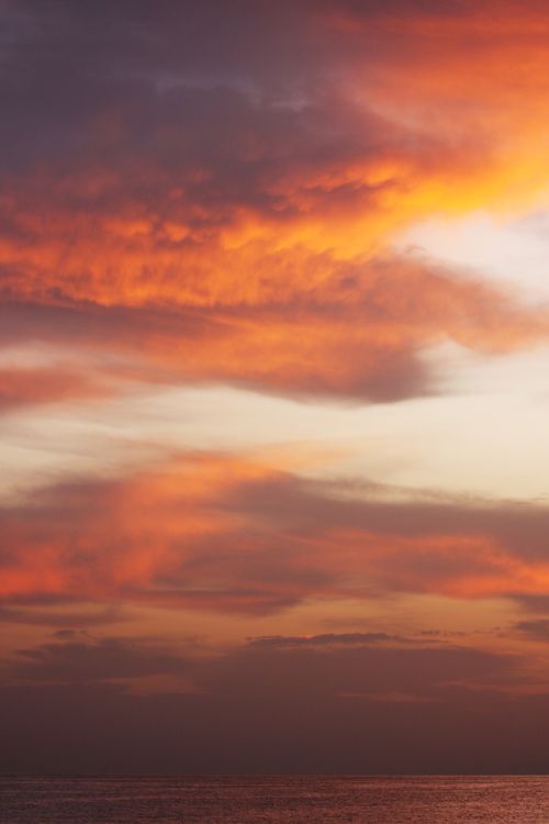 Free Dramatic sunset with vivid orange clouds over calm ocean waters. Stock Photo