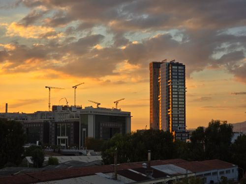 Free A modern city's skyline at sunset with skyscrapers and construction cranes under dramatic clouds. Stock Photo