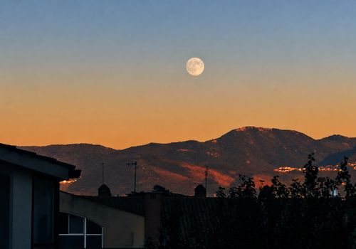Free Serene scene of a full moon rising above mountain peaks against a dusk sky. Stock Photo