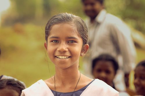 Free Cheerful schoolgirl smiling outdoors in a rural village with classmates in the background. Stock Photo