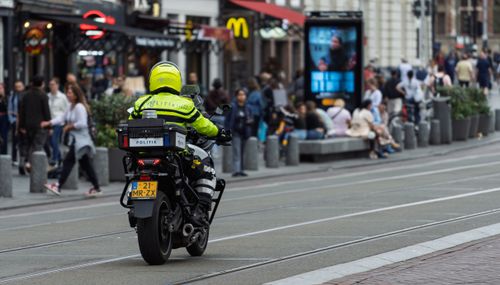 Free Police officer on motorcycle patrolling a busy city street with pedestrians. Stock Photo