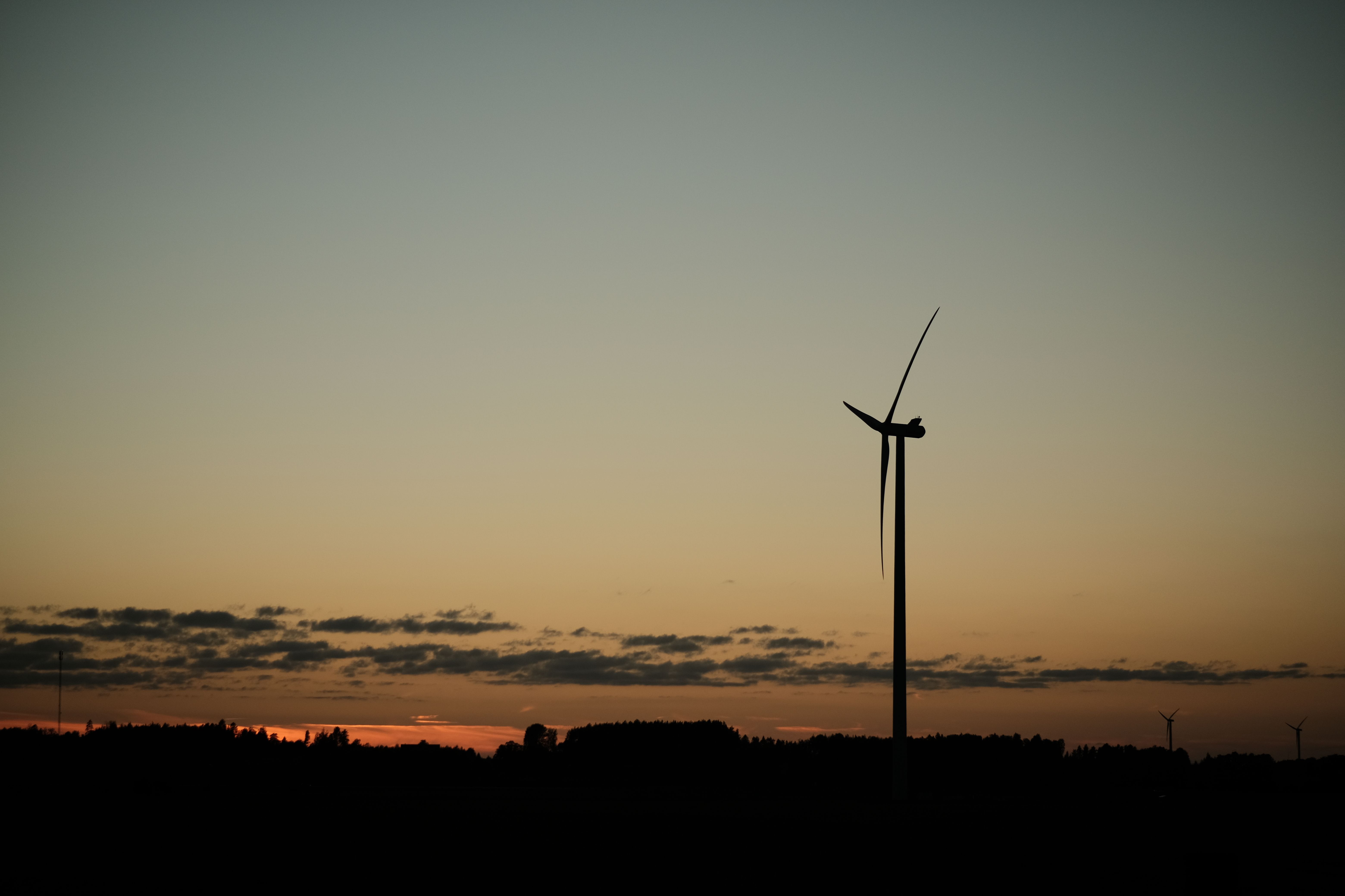 A solitary wind turbine stands against a colorful sunset, symbolizing renewable energy.