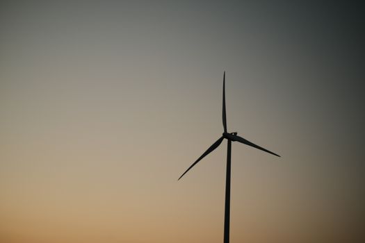 A solitary wind turbine silhouetted against a serene sunset sky, symbolizing renewable energy.