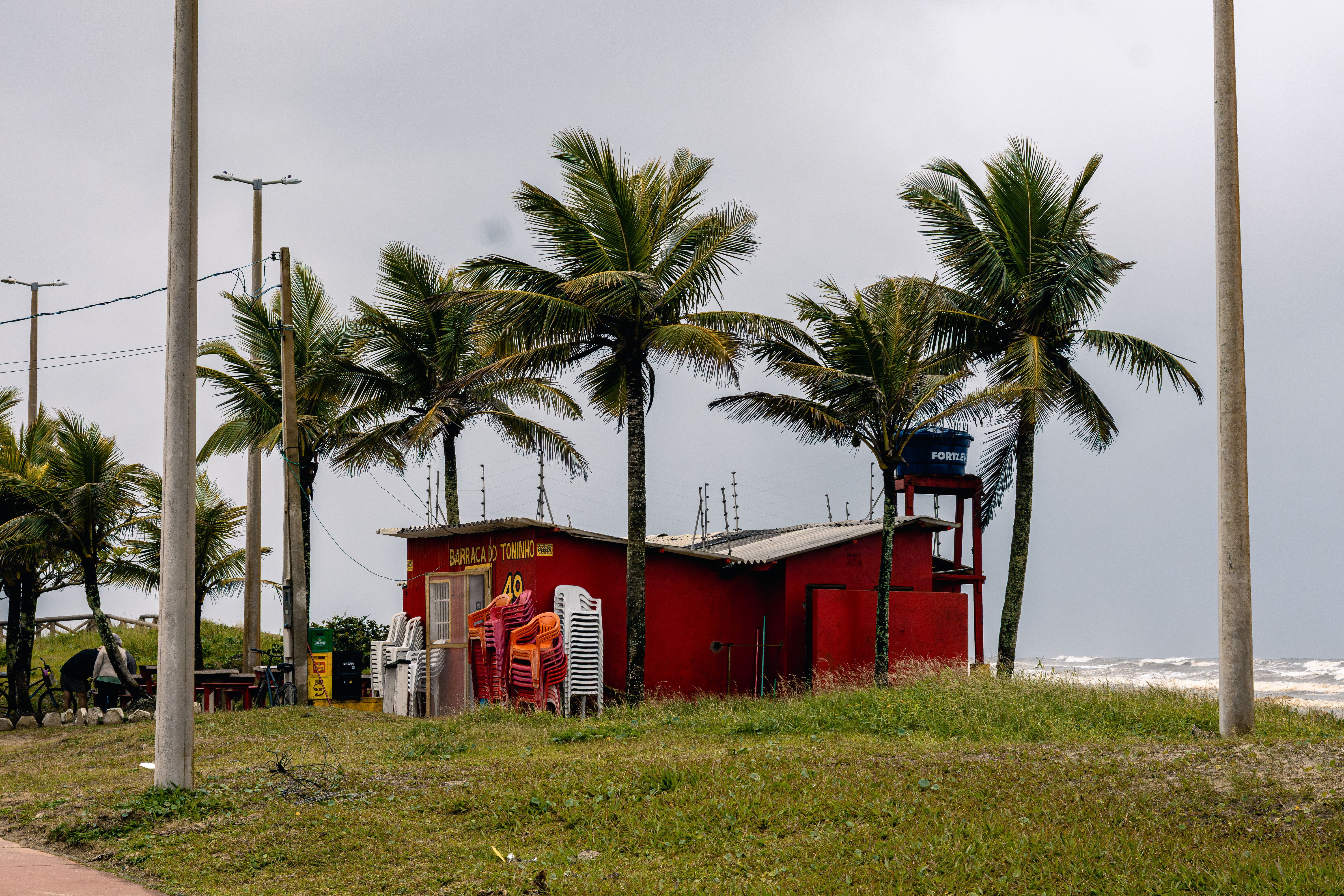Rustic beach kiosk with palm trees and stacked chairs in Peruíbe, São Paulo, Brazil.