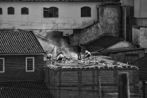 Free Black and white image of workers on a rooftop in an urban setting, suggesting construction work. Stock Photo