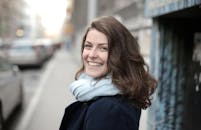 一位戴着围巾、面带微笑的女子在白日里城市热闹街道上的肖像