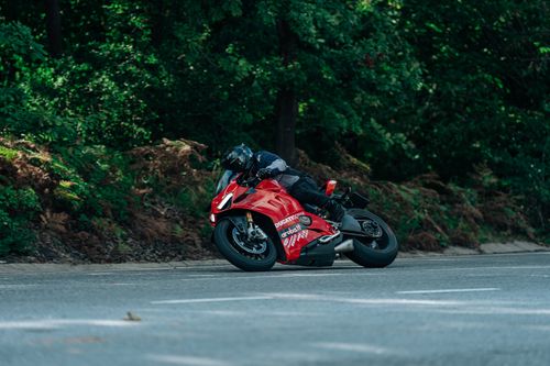 Free Red Ducati motorcycle leaning into a curve on a forest road during a competitive ride. Stock Photo