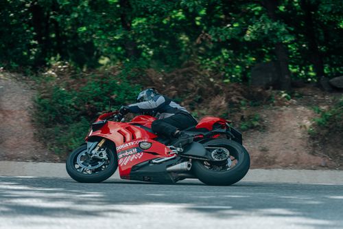 Free Motorbike rider on a red Ducati taking a sharp turn on a forested mountain road. Stock Photo