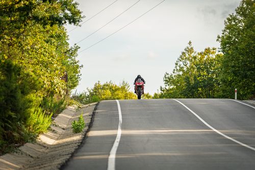 Free A motorcyclist cruises on a scenic rural road surrounded by lush green trees, embodying adventure and freedom. Stock Photo