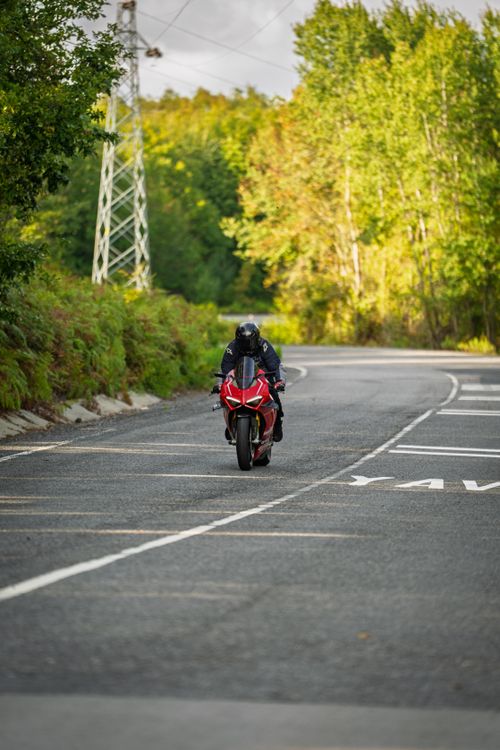 Free A motorcyclist rides a red Ducati on a scenic rural road surrounded by green trees. Stock Photo