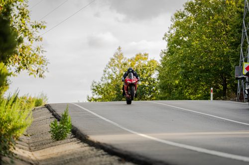 Free A motorcyclist riding a red sports bike on a scenic road surrounded by green trees. Stock Photo