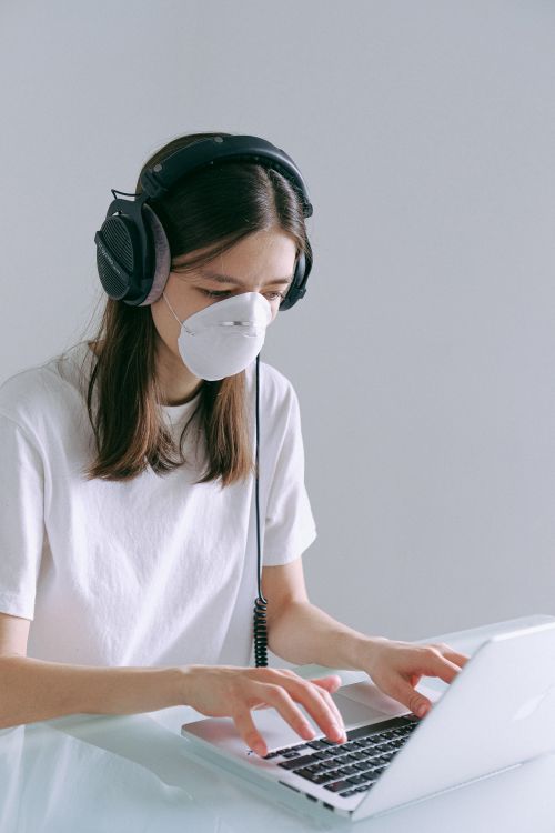 Free A woman with headphones and a mask working remotely on a laptop at home during the pandemic. Stock Photo