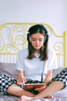 Woman in headphones using tablet on bed for remote work at home.