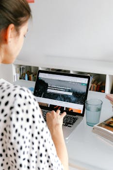 Woman working on a laptop at her home office with books and a glass of water nearby.