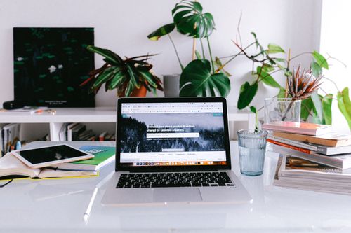 Free A clean and bright home office desk with a laptop, books, and plants, perfect for freelancers or remote work. Stock Photo