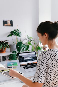 Woman working in a stylish home office with laptop and tablet, embracing remote work lifestyle.