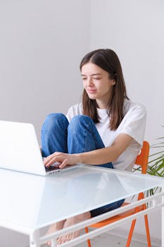 A woman sits casually with a laptop in a bright home office, embodying remote work lifestyle.